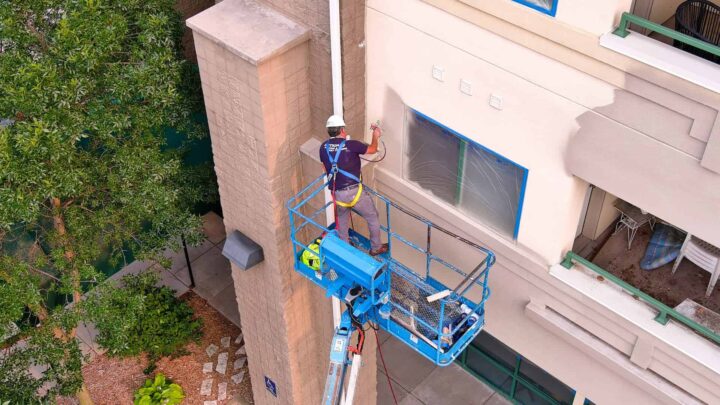 Commercial painter on hydraulic lift applying spray paint to exterior wall of a multi-story building