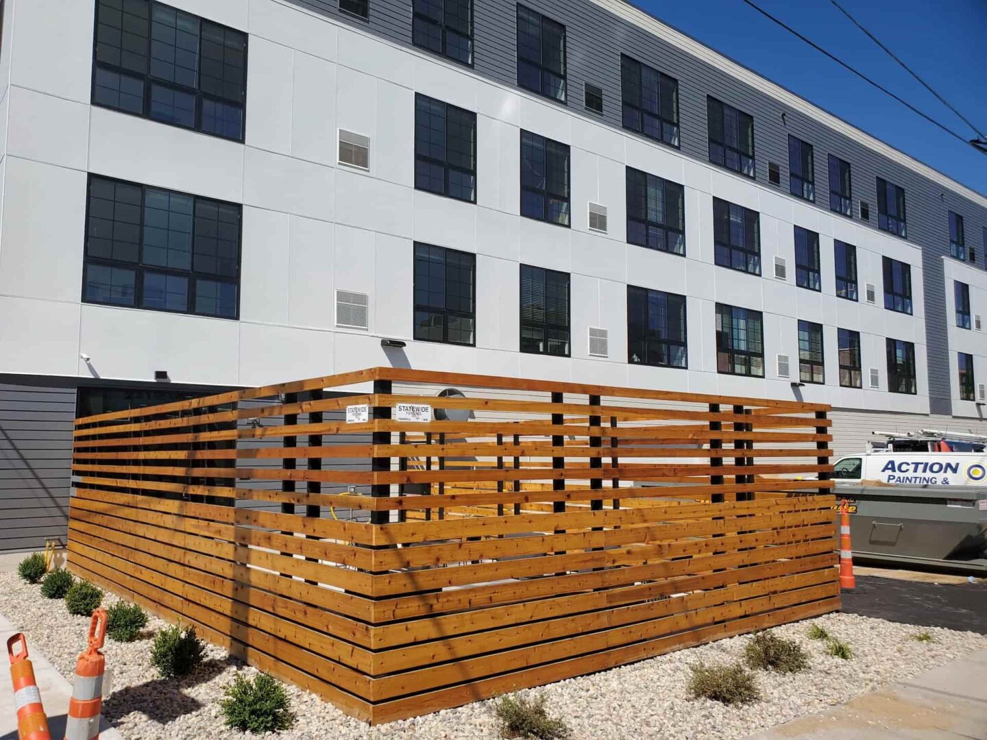 Stained horizontal wood privacy fence in front of a new apartment complex in Appleton, with an Action Painting van parked nearby