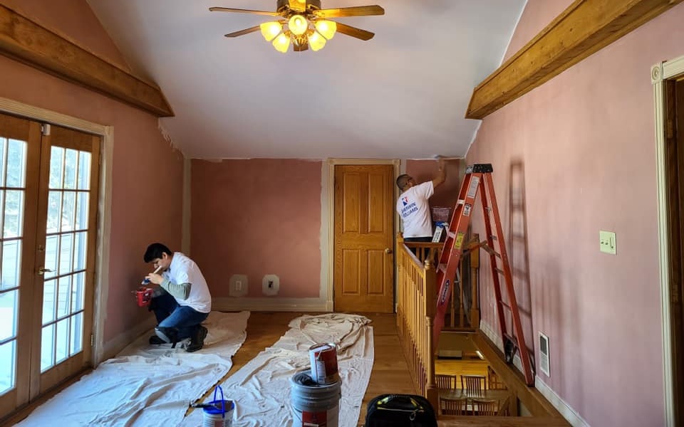 Before repainting: loft space with pink walls, exposed beams, and wood trim during active prep and paint work