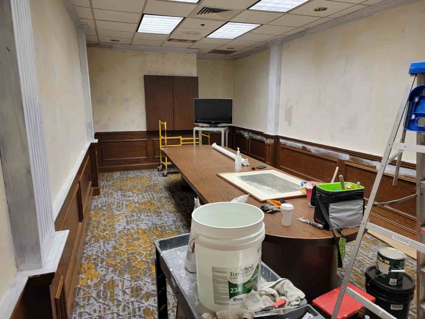Interior view of a boardroom undergoing prep work before commercial painting, with tools, ladders, and primer visible