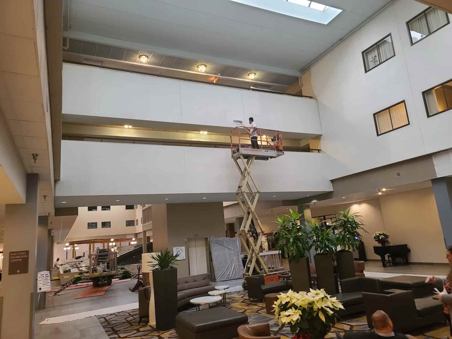 Painter applying fresh white paint in a commercial hotel lobby using a scissor lift at Fox Cities Hilton
