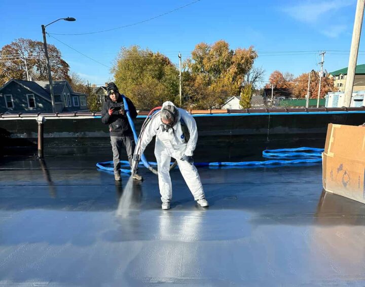 Technician applying polyurea roof coating with spray equipment during commercial building project