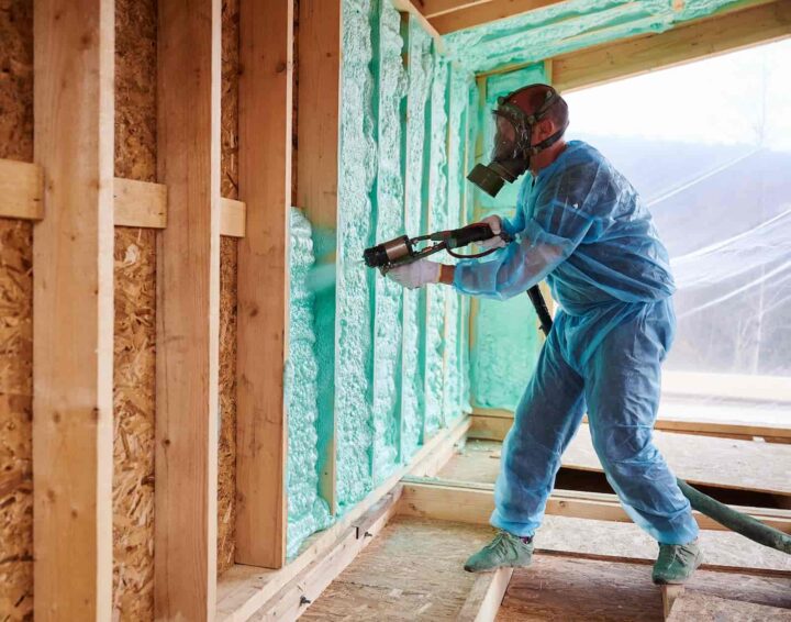 Worker applying spray foam insulation to interior wall framing during construction
