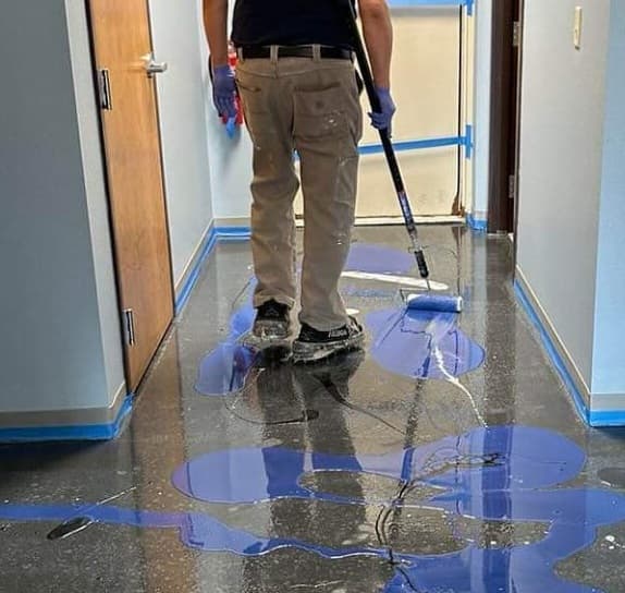 Technician applying epoxy floor coating with a roller as part of the installation process